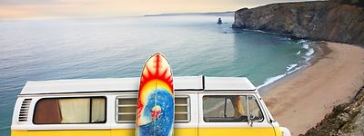 A yellow van with a surf board at the beach